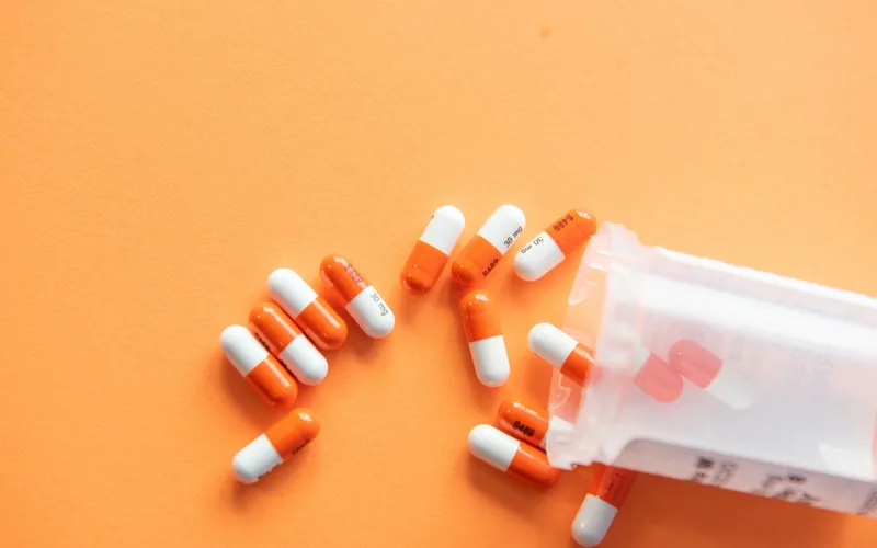 Geöffnete Tablettendose mit orange-weißen Kapseln auf orangefarbenem Untergrund